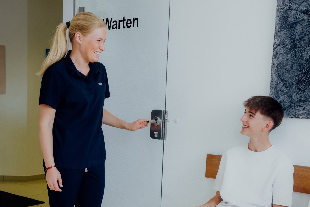 Dr. Charlotte Zimmermann öffnet die Tür zum Wartezimmer und begrüßt einen jungen Besucher